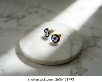 A pair of charming circular cloisonné stud earrings, featuring a distinct white flower on a rich blue background, displayed on a white marble surface.