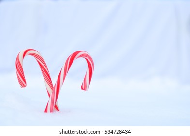 Pair Of Crossed Red And White Striped Candy Canes In Snow With White Background