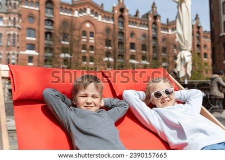 Pair of cute adorable little children enjoy having fun chilling on vintage deckchairs seats on sunny day Hafencity quarte in old Hamburg city center warm sunny day. Chilling lounge chairs on street