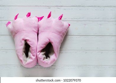 Pair Of Cute Pink Monster Foot Slippers With Big Claws On White Wooden Background. Copy Space. Top View.