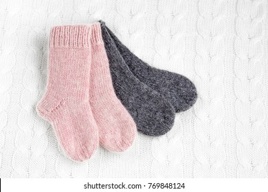 A Pair Of Cute Small Different Colored Cashmere Knitted Newborn Baby Socks On A White Woolen Background. 