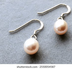 A pair of delicate sterling silver hook earrings, each adorned with a lustrous pale pink pearl. Perfect for adding a touch of understated elegance.