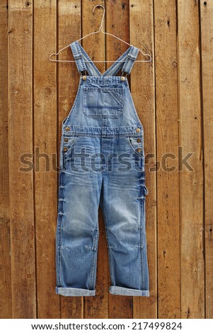 Pair of denim dungarees hanging against wooden wall 