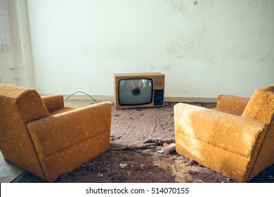 Pair of disused yellow sofa chairs in front of broken old tube style TV in abandoned house with torn carpeting - Powered by Shutterstock