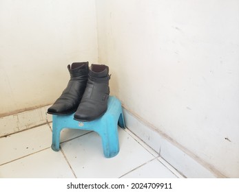 A Pair Of Dull Black Loafers Sitting On A Small Blue Plastic Stool In The Corner Of The Room