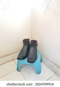 A Pair Of Dull Black Loafers Sitting On A Small Blue Plastic Stool In The Corner Of The Room