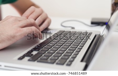 pair of dynamic hands typing and scrolling on a laptop computer working, designing, comunicating and researching, computer with an external hard drive USB connected on a table. 