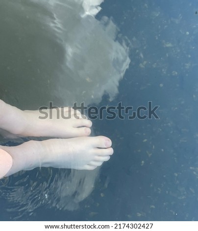 A pair of children’s feet dipping their toes into a river which has the reflection of a fluffy white cloud in it