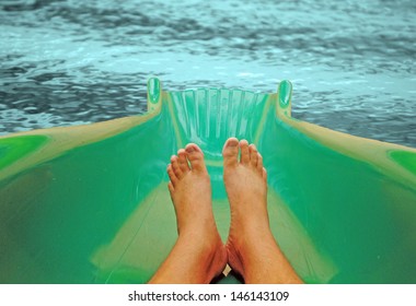 A pair of feet on a water slide about to land in a refreshing pool