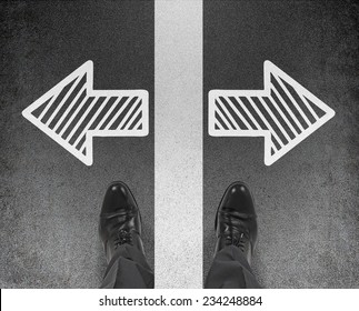 A Pair Of Feet Standing On The Road With Drawn Arrows In Two Different Directions. Decision Making Concept. 