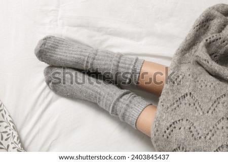 Pair of female legs wearing cozy grey cashmere socks under blanket in bed, closeup