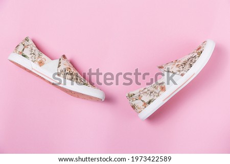 Pair of female's new stylish slip-ons with floral ornament on a pink background. Flat lay. Copy space. Side view of shoes.