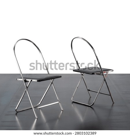 pair of folding chairs, featuring a chromed metal frame and black leather seat.