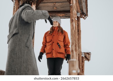 A pair of friends interact cheerfully while surrounded by snow and timber, encapsulating the joy and excitement of wintertime outdoors in a rustic environment.