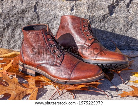 A pair of genuine leather boots on fall autumn leaves with a stone background.