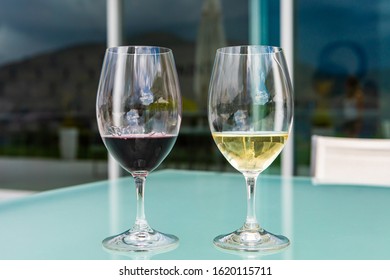 Pair Of Glasses On Glass Table Close Up, Selective Focus View, Two Wine Glasses Filled Of Dark Red And Golden White Wines, Winery Luxury Tasting Room