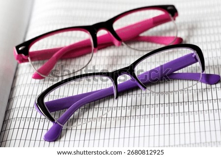 A pair of glasses with pink and purple frames on documents in an office.
