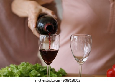 Pair of glasses for red wine woman pouring in kitchen. Romantic dating couple cooking salad for dinner, drinking alcohol, celebrating Valentines day, anniversary. Love, romance concept. Close up - Powered by Shutterstock