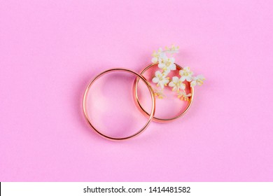 a pair of gold wedding rings and small white flowers in a ring on a pink background, top view flat lay