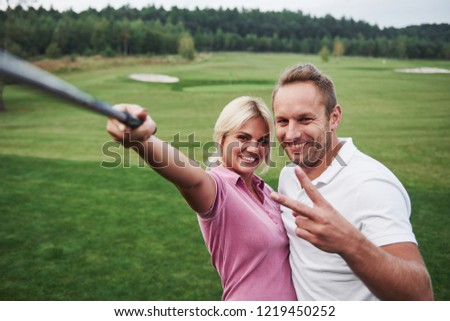 A pair of golfers make a photo on the golf course using a stick like a sephi pole.