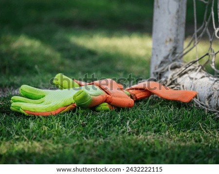 A pair of green and orange goalkeeper gloves next to a goal post