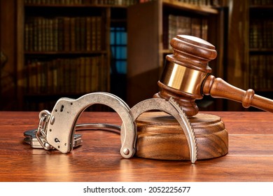 A pair of handcuffs rests against a judge's gavel and block in a judge's law chamber.  For inferences regarding public safety, crime, law and punishment. Copy space set aside on the upper left.