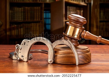 A pair of handcuffs rests against a judge's gavel and block in a judge's law chamber.  For inferences regarding public safety, crime, law and punishment. Copy space set aside on the upper left.

