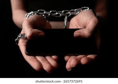 A pair of hands chained together while holding a smartphone. The concept of obsession and dependence on digital gadgets and social media.