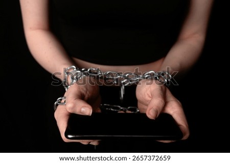 A pair of hands chained together while holding a smartphone. The concept of obsession and dependence on digital gadgets and social media.