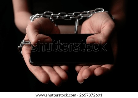 A pair of hands chained together while holding a smartphone. The concept of obsession and dependence on digital gadgets and social media.