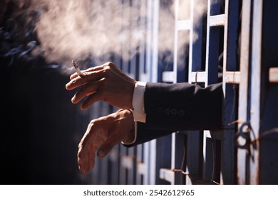 A pair of hands holding a cigarette appears behind blue prison bars, evoking themes of confinement, isolation, and the struggle for freedom in a dramatic way. - Powered by Shutterstock