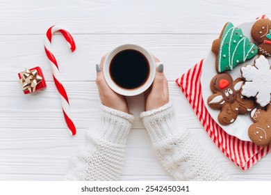 A pair of hands holding coffee on a festive table with gingerbread cookies, candy cane, and a gift. Perfect depiction of a cozy Christmas morning, warmth, and holiday spirit. - Powered by Shutterstock