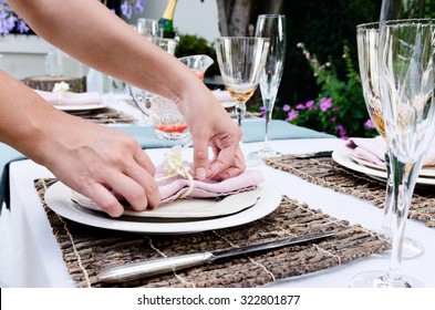 Pair Of Hands Making Final Adjustments To A Napkin For A Simple Rustic Country Style Table Setting, A Party Gathering In A Casual Outdoor Garden Setting