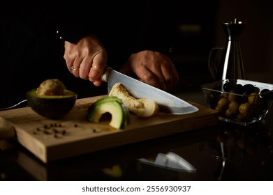 A pair of hands slice bread on a wooden board, surrounded by fresh avocado. The scene captures culinary preparation with a focus on healthy ingredients and home cooking.