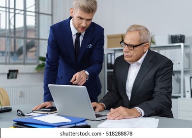 Pair Of Handsome Young And Mature Business Men Discussing Something On Laptop Computer At Desk In Office