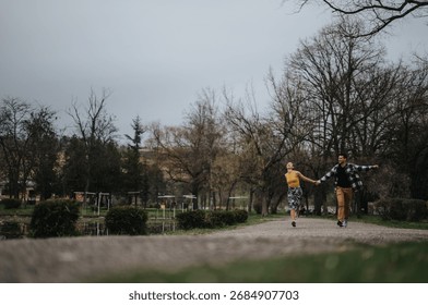 A pair holding hands while walking on a path surrounded by trees and nature.