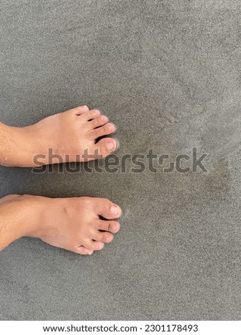 A pair of human feet on the gray beach sand. Bare feet with 10 toes complete.