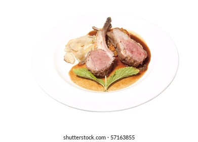 pair of lamb chops with a sprig of mint on a ginger and mango chipolte sauce on a white plate, isolated on a white background