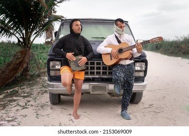 A pair of latin musicians are playing spanish guitar and cajon drum in front of his caravan during a road trip