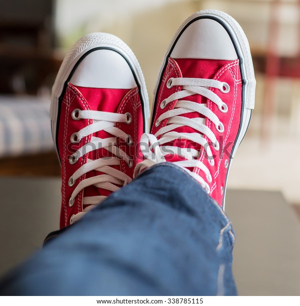 Pair\
of legs crossed with feet wearing red converse\
shoes