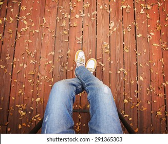 A Pair Of Legs Taken From Overhead On A Deck With Leaves That Have Fallen 