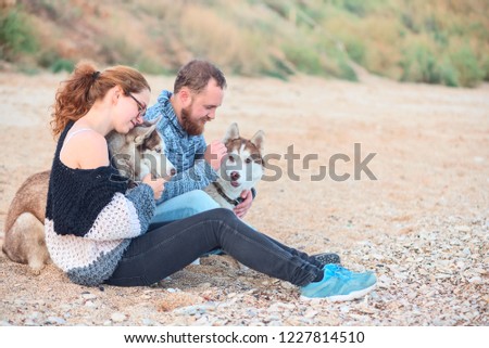 Pair of lovers sitting on the sand on the beach with husky dogs
