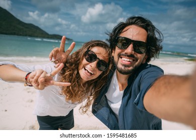 A pair of lovers take a selfie on a tropical beach. The guy and the girl cheerfully smile at the phone camera on the background of the sea. Newlyweds and tropical lagoon with green mountains 