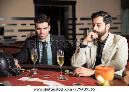 Pair of men looking serious while drinking champagne and playing cards in a casino