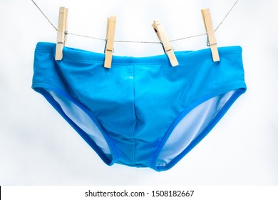 A pair of men's cyan swim briefs hanging on four clothespins.
