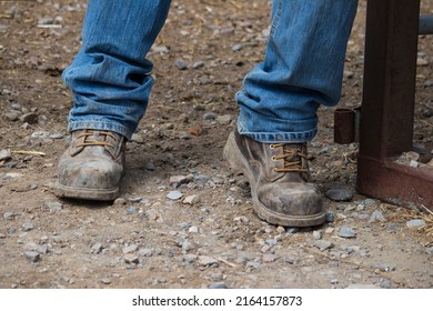 Pair Of Men's Worn Work Boots And Denim Jeans Standing In The Dirt.