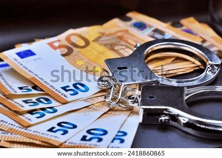Pair of metal police handcuffs on Euros banknotes money cash background. Corruption, dirty money, gambling or financial crime ideas concept.