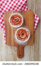 Pair of Mini Apple Rose Shaped Tartlets Sprinkled with Powder Sugar on a Wooden Breadboard