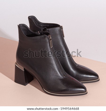 Pair of new black women short boots on medium high heels on beige background studio shot.