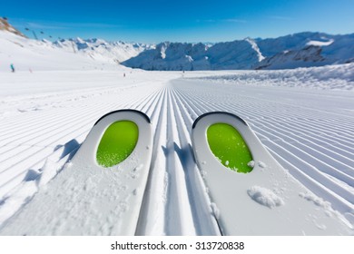 Pair Of New Skis Standing On The Fresh Snow On Newly Groomed Ski Slope At Ski Resort On A Sunny Winter Day.